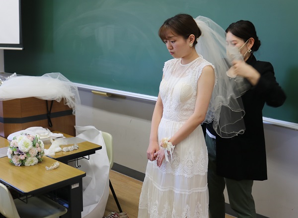 ブライダルビジネスがテーマの授業で、受講生が実際にウェディングドレスを身に付けて衣装について学びました